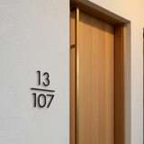Modern house number '13 107' on a textured wall with a wooden door.