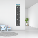 A vertical wall-mounted height chart with measurement markings in centimeters and meters, shown hanging on a white wall in a bright modern room with a chair, side table, plant, and rug.