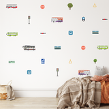 Bus-themed wall decals displayed on a white wall above a bed in a child's bedroom. The decals feature various illustrated buses, stop signs, traffic lights, trees, and transit icons in muted pastel and bright colors.